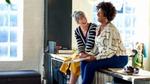 Twee vrouwen die op een werkbank zitten te praten en lachen