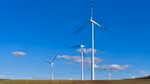 Een rij windturbines staat in een omgeploegd veld, tegen een helderblauwe lucht